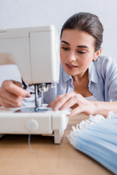 Smiling seamstress sewing medical mask on machine  - Foto, immagini