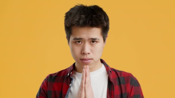 Ázsiai Guy imádkozó összecsukható kezek imában gesztus, sárga háttér - Felvétel, videó
