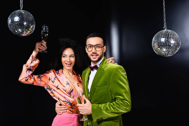 positive multiracial couple drinking champagne on black background - Photo, Image