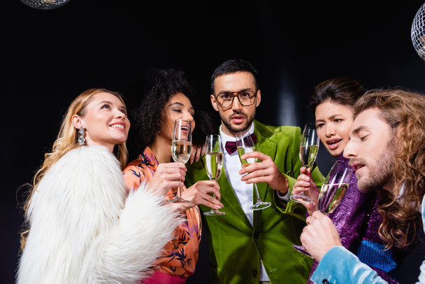 pozitivní mezirasové přátelé pití šampaňské na černém pozadí - Fotografie, Obrázek