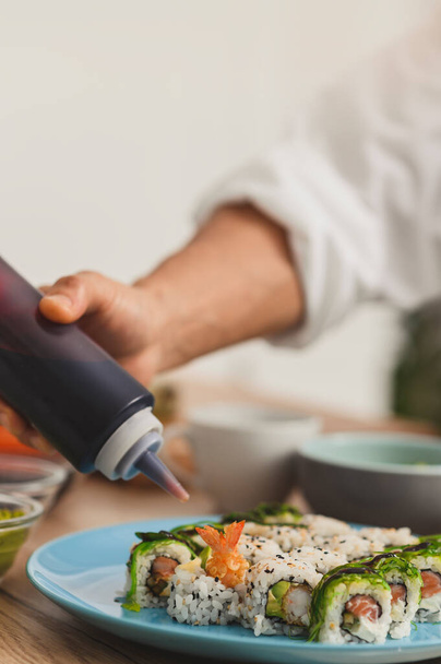 Close-up männliche Hand mit Flasche fügt Sauce auf Sushi-Teller. Konzept der Essensausgabe - Foto, Bild