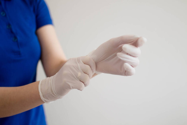 Genç bir kadın eline tek kullanımlık beyaz bir tıbbi eldiven takıyor. Mavi tişört giyen bir kadın. Güzellik koruması, güvenli temizlik konsepti.. - Fotoğraf, Görsel