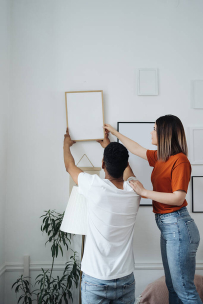 Mixed race ethnicity millennial couple holding frame admires painting or photo - Photo, Image