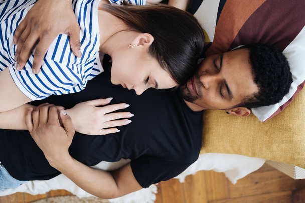 Young diverse couple lying on a couch at home resting - Photo, Image