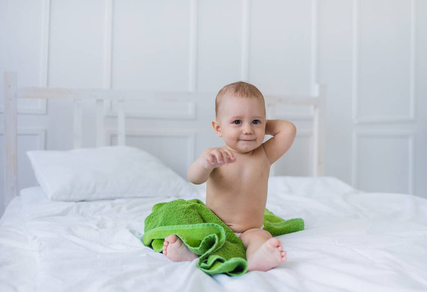 a baby boy with brown eyes sits on the cotton bedding on the bed and looks at the camera - Photo, Image