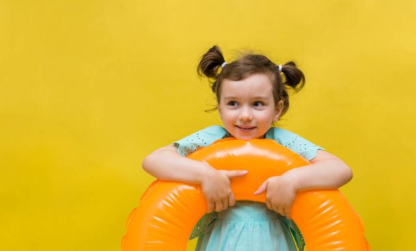 portrait of a little girl holding an inflatable circle on a yellow background with space for text. Summer child - Photo, Image