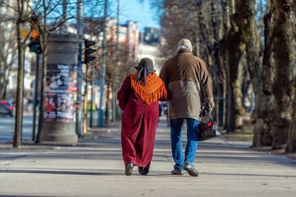 A couple of eldery people in hands are walking through the city street. Rear view. - Foto, Imagem