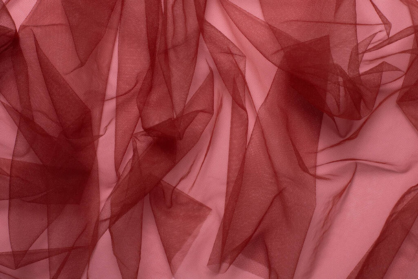 Textura de tejido de tul rojo arrugado y arrugado sobre un fondo rosa de cerca. fondo para su maqueta - Foto, Imagen