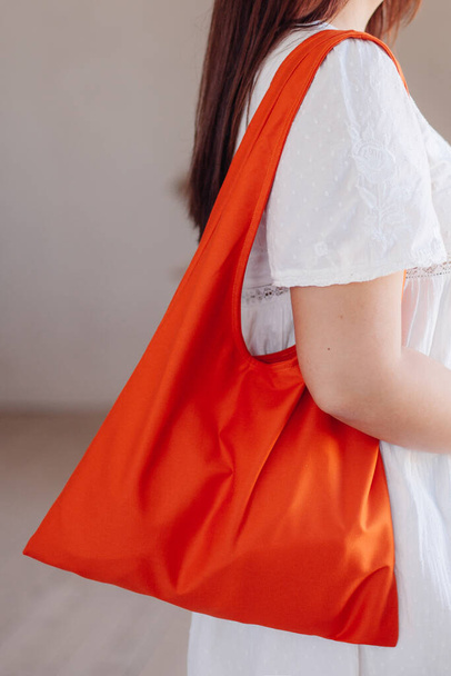 Młoda dziewczyna w białej sukience trzyma pomarańczową bawełnianą torbę na ramieniu. koncepcja świadomej konsumpcji, ochrony środowiska. - Zdjęcie, obraz
