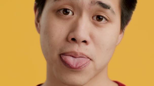 Ázsiai Guy kilóg nyelv néz kamera, sárga háttér - Felvétel, videó