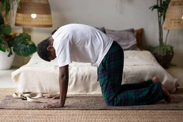 Sporty muscular young african man working out, yoga, pilates, fitness training, doing Cat Pose - Foto, Imagen