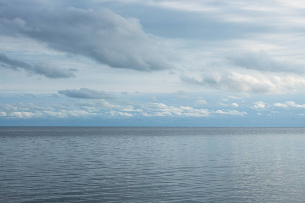 Panoramablick auf blaues Meer und klaren Himmel mit bunten weißen Wolken. Natur, Klimawandel, Reflexionen der Symmetrie auf dem Wasser bei Tageslicht. Die Idee, sich ruhig, cool und entspannend für den Hintergrund, Attrappen, Poster, Vorlagen und Kopierraum zu fühlen. - Foto, Bild