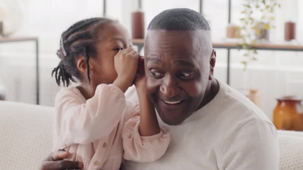Portré kis afrikai lány gyermek lánya kisgyermek óvodás ül felnőtt férfi érett afro fekete nagypapa etnikai apa suttog mondja titkos fül megosztása titoktartás pletyka férfi mondja wow - Felvétel, videó