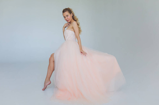 Middle age blond lady in pink dress posing on gray background. - Photo, Image