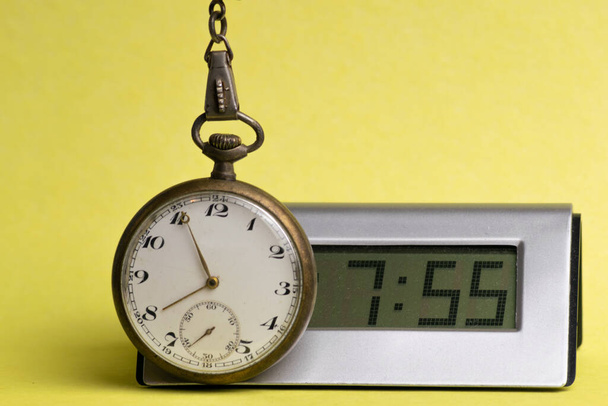 Antyczny zegarek kieszonkowy obok nowoczesnego zegarka cyfrowego na żółtym tle - Zdjęcie, obraz