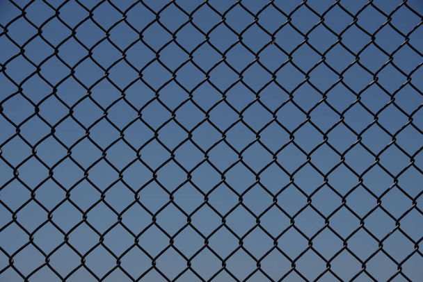 Marco completo vista de cerca de un segmento de una cerca de eslabón negro con cielo azul detrás - Foto, Imagen