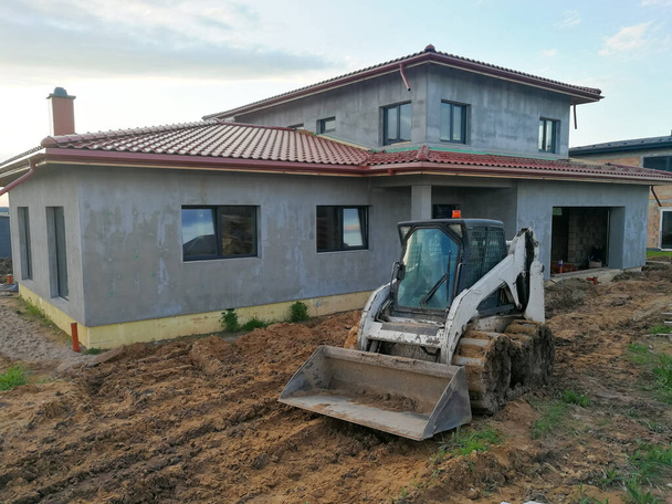 Piccolo bulldozer di lavoro a terra in cantiere di fronte alla singola casa in costruzione - Foto, immagini