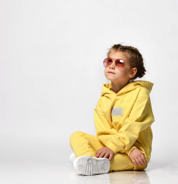 Portrait of a stylish little girl sitting and looking at the camera on a white background. - Φωτογραφία, εικόνα