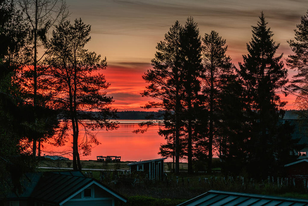 日没後の風光明媚な赤オレンジ色の燃焼真夜中の空の近くのビュー。夏の半ばに近い光の夏の夜。湖の美しい色の空の反射。スウェーデン北部、ウメア。夏時間 - 写真・画像