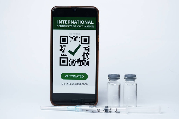 Uma foto de smartphone com falso Certificado Internacional de Vacinação nele, duas doses de vacina e insight seringa de injeção. 2 doses de vacina necessárias para a imunização. - Foto, Imagem