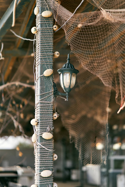 Linterna cuelga de un pilar trenzado con aparejos de pesca bajo un dosel con una red de pesca - Foto, imagen