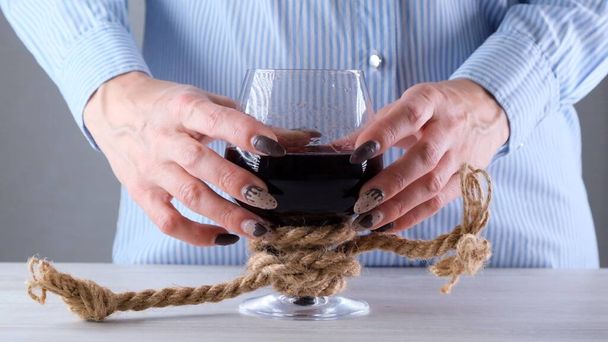 ワイングラスを持ってる女の手はロープで縛られてる。アルコール依存の概念。アルコール依存症の治療の問題 - 写真・画像