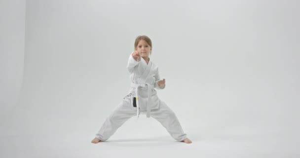 Ta holka doma cvičí karate. Dítě je oblečené v kimonu na bílém pozadí. - Záběry, video