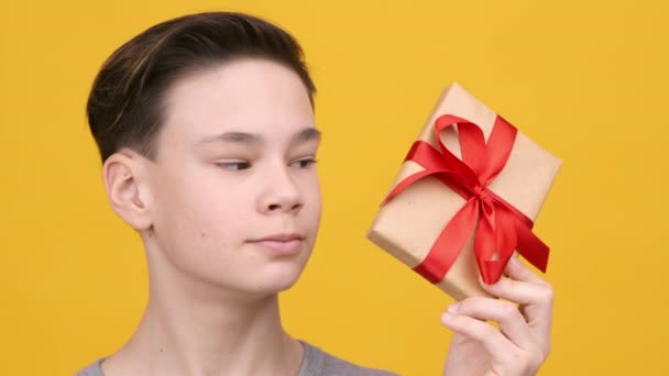 Teenager Boy Holding Wrapped Present Posing πάνω από κίτρινο φόντο - Πλάνα, βίντεο