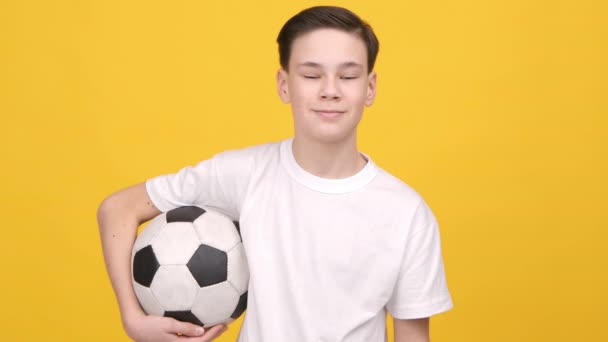 adolescente chico posando celebración fútbol bola de pie sobre amarillo fondo - Metraje, vídeo