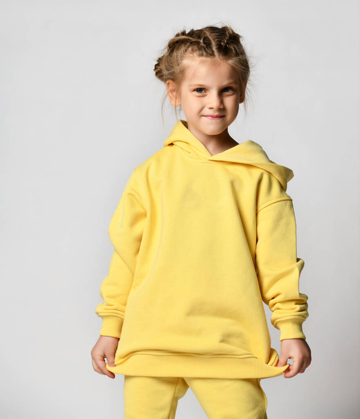 cute obedient preschool girl, modestly posing on a light background in a yellow hoodie with a hood. - Photo, Image