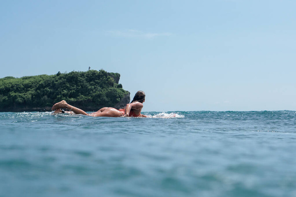 Young woman with beautiful body in swim suit surfer on surf board in blue ocean in Balangan surf spot in Bali - Foto, Imagen