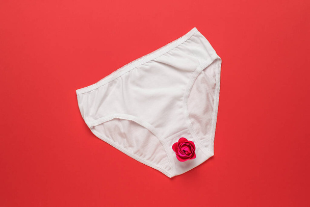 Bílé dámské kalhotky s červeným růžovým pupenem na červeném pozadí. Překvapení. Plocha. - Fotografie, Obrázek