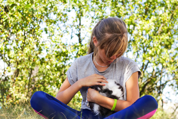 Defocus blonde little girl holding and caress cat, black and white small beautiful kitten. Nature green summer background. Girl holding and stroking pet, talk it. Love animals concept. Out of focus - Photo, Image