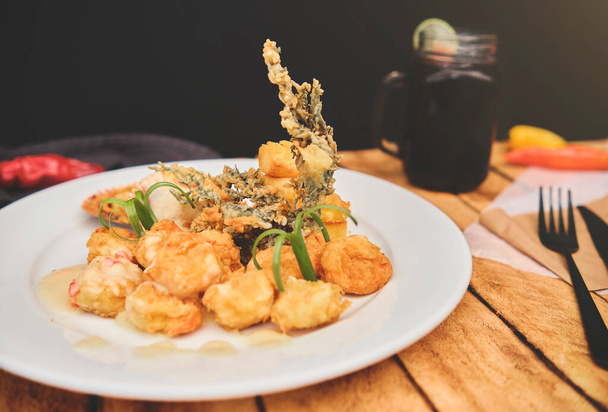 Nourriture péruvienne : Crevettes sautées aux herbes et à l'ail, table en bois, servies sur une assiette blanche, accompagnées de jus de maïs violet - Photo, image