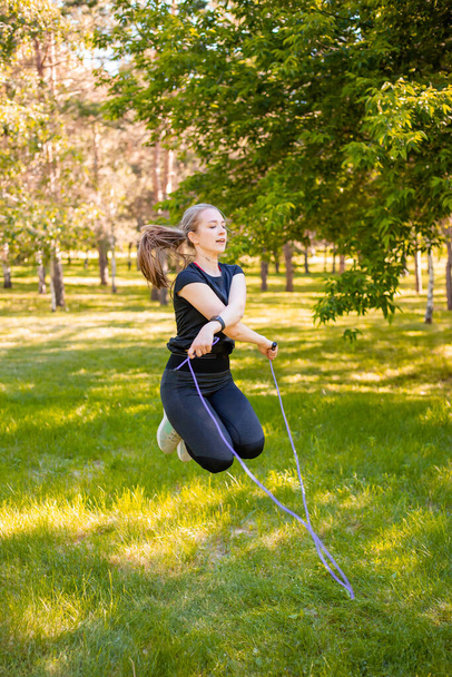 Young woman jumping rope on the lawn in a summer park. Jumping model. The concept of a healthy lifestyle and outdoor sports. - Fotografie, Obrázek
