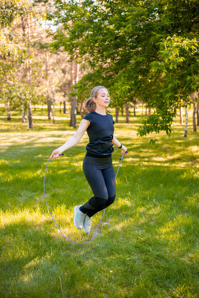 夏の公園で芝生の上でロープをジャンプ若い女性。ジャンプモデル。健康的なライフスタイルとアウトドアスポーツのコンセプト. - 写真・画像
