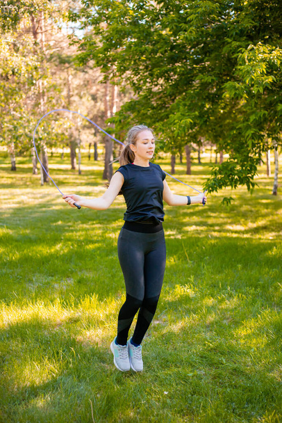 Mujer joven saltando la cuerda en el césped en un parque de verano. Modelo de salto. El concepto de un estilo de vida saludable y deportes al aire libre. - Foto, Imagen