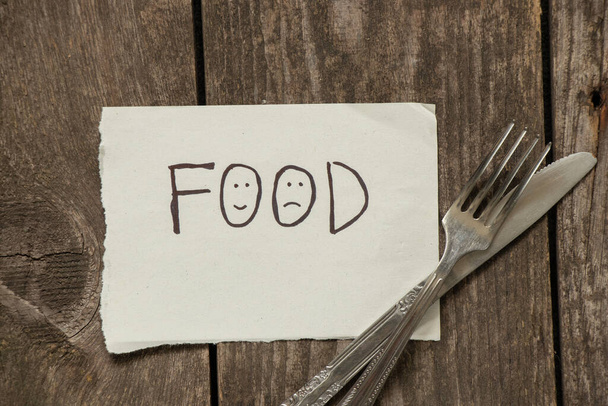 a comida de inscrição em uma folha de papel ao lado de um garfo e faca está em uma mesa de madeira velha - Foto, Imagem
