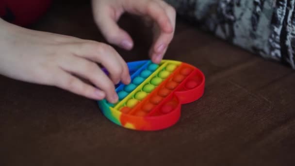 παιδί παίζει με παιχνίδι ποπ απλό λακκάκι κοντά καρδιά σχήμα στον καναπέ - Πλάνα, βίντεο