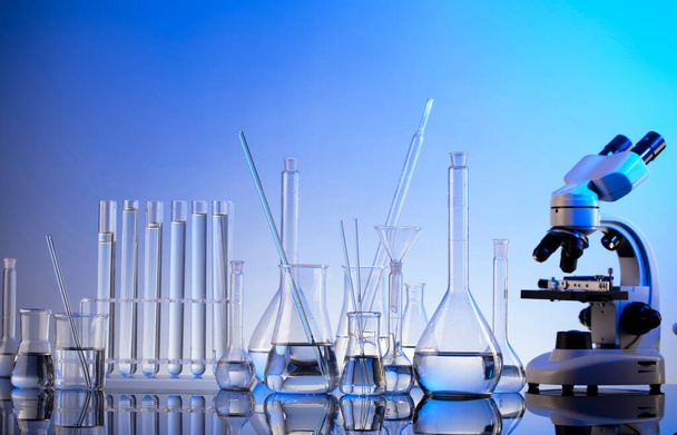 Лабораторные исследования. Микроскоп, стеклянные трубки и стаканы на синем фоне. - Фото, изображение