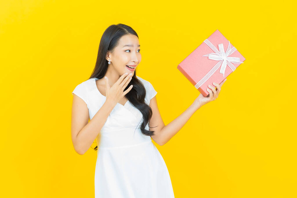 Portrait beautiful young asian woman smile with red gift box on yellow color background - Fotó, kép