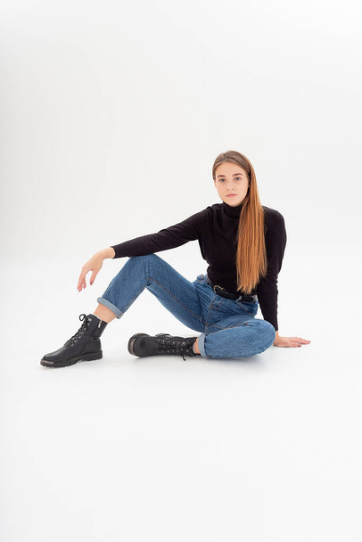 young attractive caucasian woman in black turtleneck, blue jeans at white studio - Фото, изображение