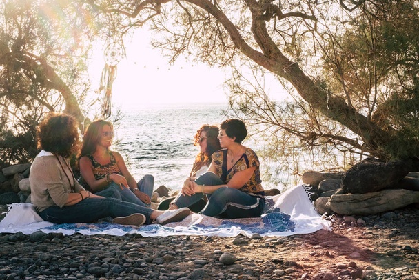 Ryhmä naisia ystävien istua yhdessä kiviä rannalla nauttia ystävyydestä hymyillen ja puhuen kirkas taivas auringonlasku taustalla luonto ulkona vapaa - Valokuva, kuva