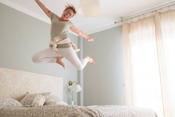Young adult pretty woman go crazy for happiness and jump on the bed with coffee cup  - 写真・画像
