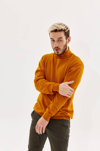 modischer blonder Mann in orangefarbenem Pullover und Hose vor hellem Hintergrund - Foto, Bild