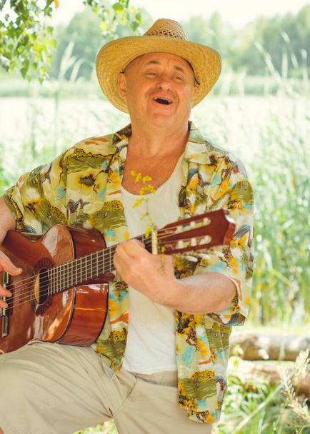 Legrační starší muž v tiskové košili turista hraje na kytaru a zpívat píseň na přírodě venku, výlet do Ameriky a potěšení pro dovolenou - Fotografie, Obrázek