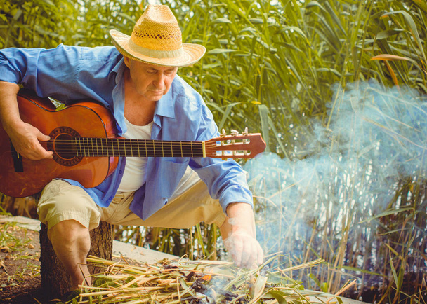 Vicces idősebb férfi nyomtatott ingben turista gitározik és énekelni dalt a természetben szabadban, utazás Amerikába és öröm nyaralni - Fotó, kép