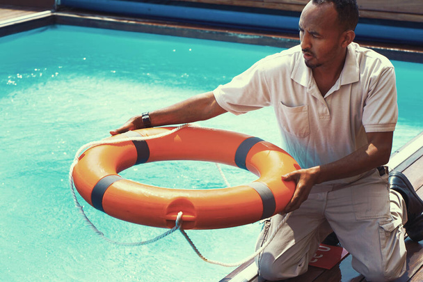 Африканский работник отеля бросает спасательный круг человеку, тонущему в бассейне. Спасение тонущего человека - Фото, изображение