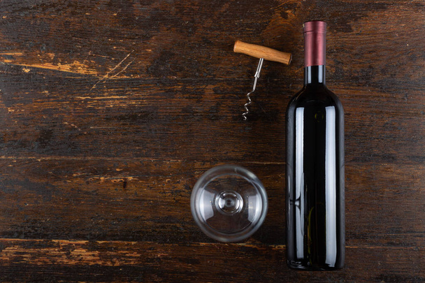 Red wine bottle with empty glass and corkscrew on a wooden background. Alcoholic drink. Top view. - Foto, Imagem