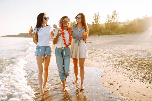 Three young woman eating pizza and have fun on the beach. Fast food concept.  Summer holidays, vacation, relax and lifestyle consept. - Fotó, kép
